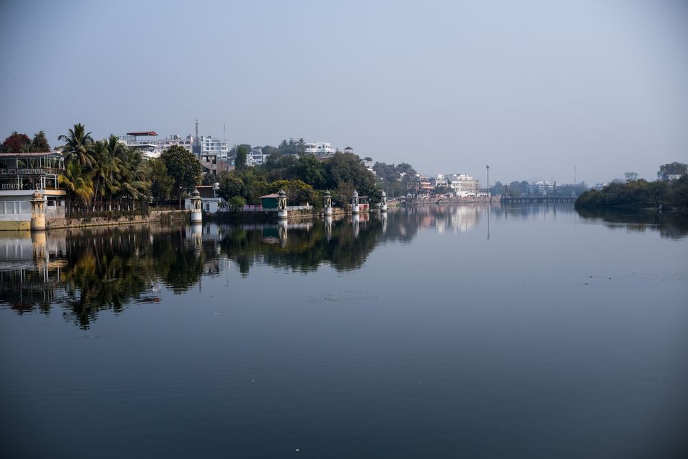 Calm river reflecting buildings and palm trees along the banks under a clear blue sky.