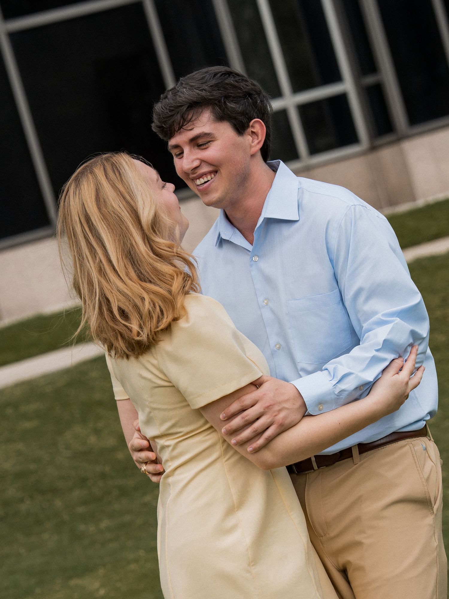 A couple in casual attire sharing a romantic moment outdoors, with a light blue shirt and khaki pants.