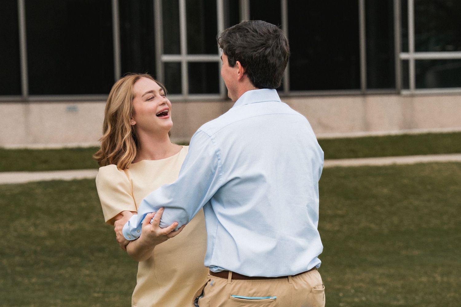 Dancing couple shares a joyful moment together on a sunny afternoon outside a glass building.