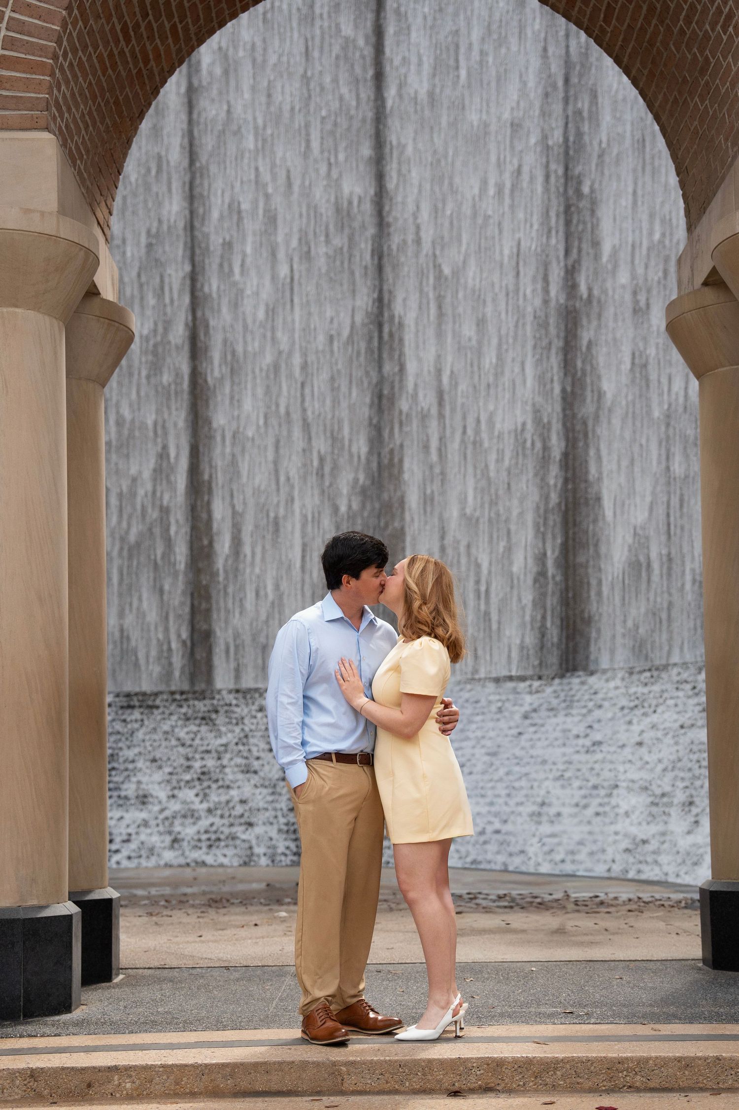 A romantic moment captured under stone archways with a textured grey wall background.