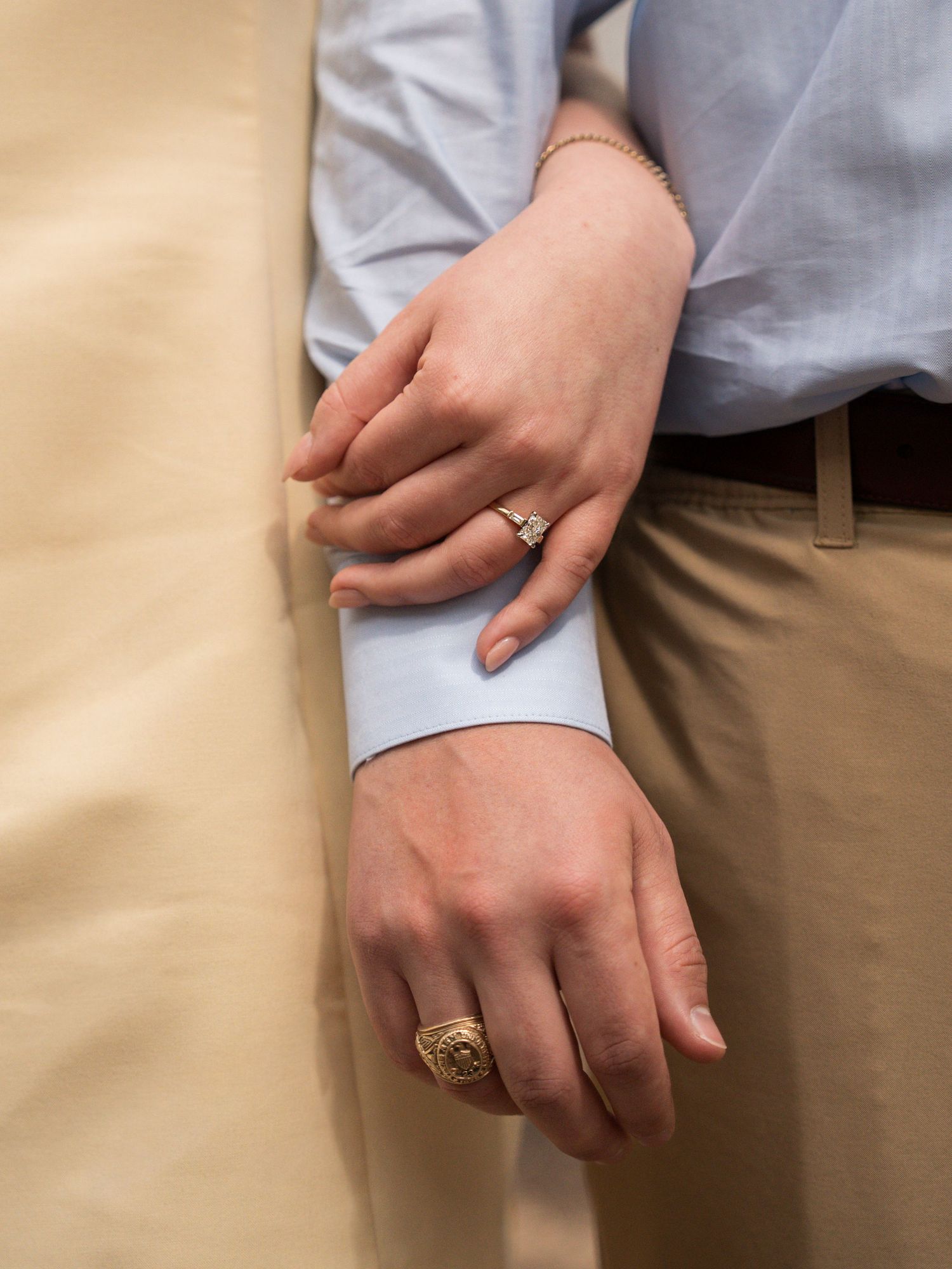 Close-up shot of hands wearing engagement rings against casual clothing.
