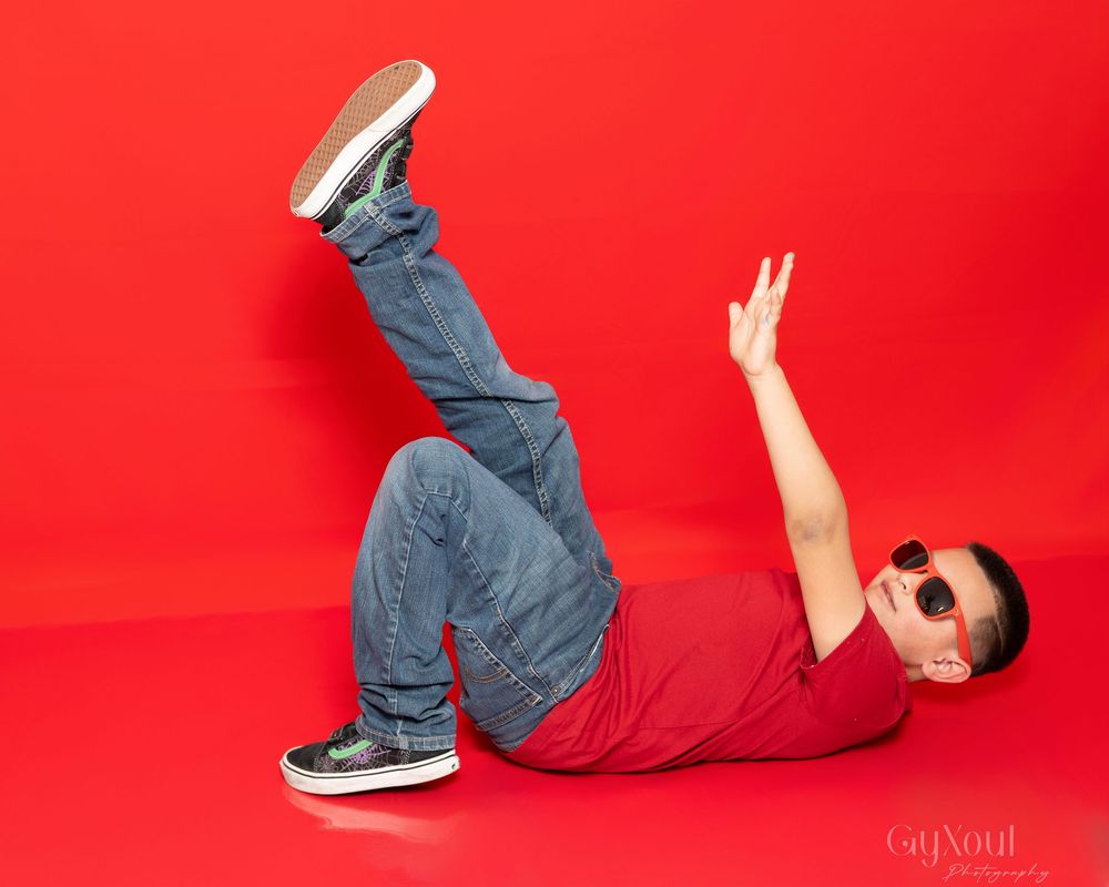 Person in red shirt and jeans performs breakdance move against vibrant red background.