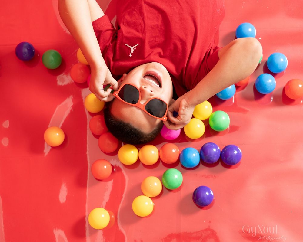 Colorful plastic balls being arranged by hands on a bright red background for sensory play activity.