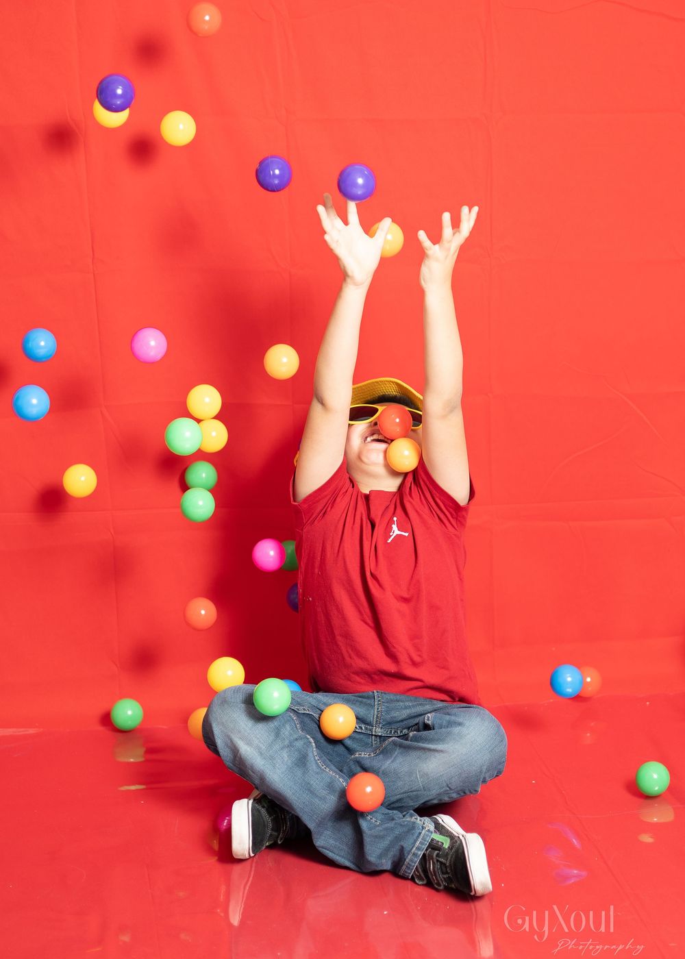 A series of playful shots against a red backdrop shows someone catching and tossing colorful plastic balls in the air.