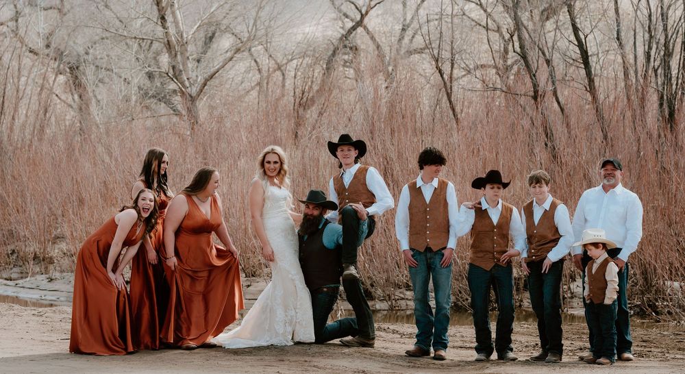 A wedding party stands in a row among bare winter trees during an outdoor ceremony.