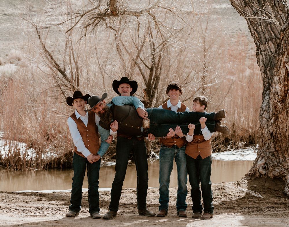A group in western attire poses together by a tree in a sepia-toned winter landscape.