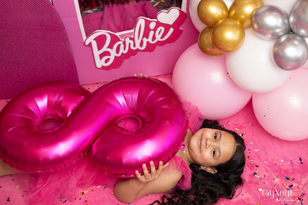 Pink and gold balloon decorations create an elegant Barbie-themed party backdrop for a photo session.