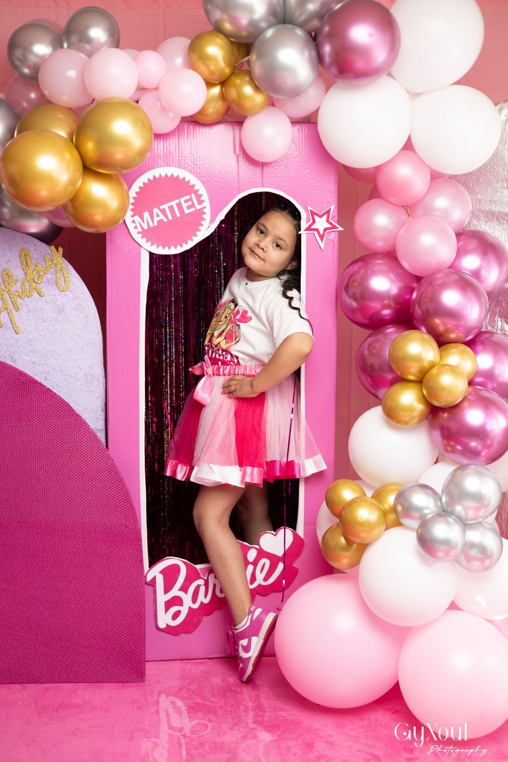 Festive Barbie-themed party setup with pink and gold balloon garland decorations against a pink backdrop.
