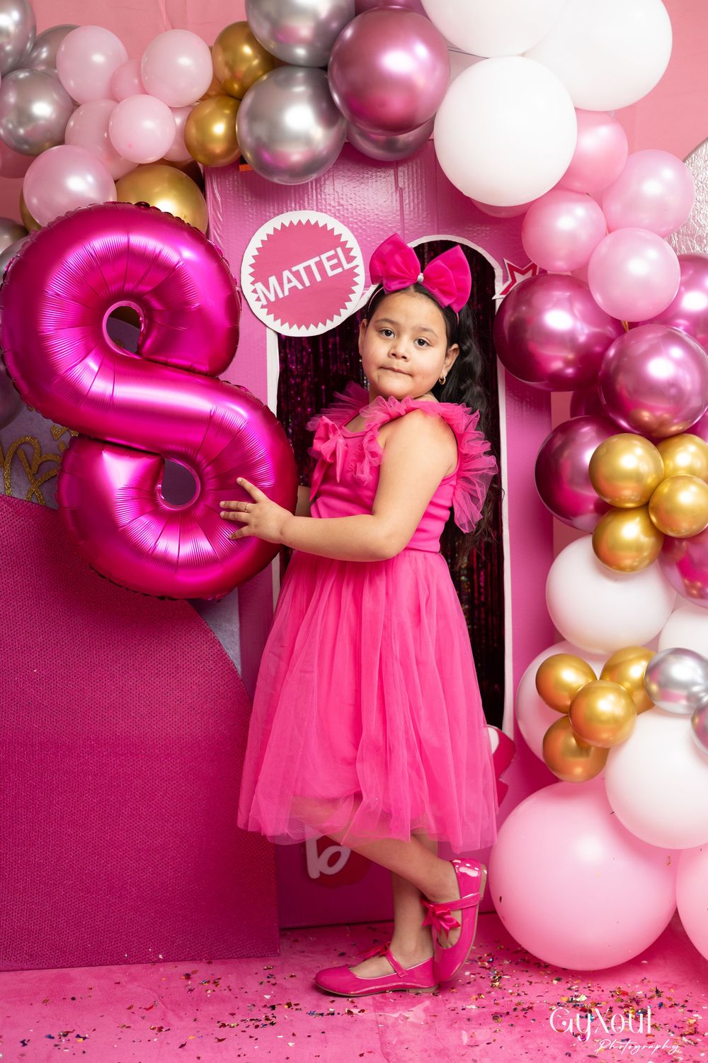 Pink and gold balloon arch display with a large metallic pink letter balloon and sparkly party decorations.