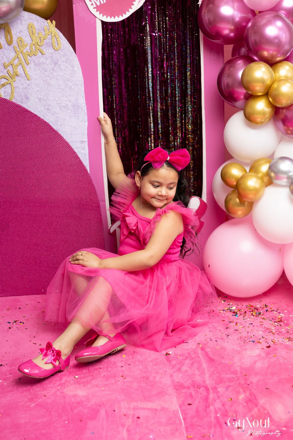 Pink tulle dress and gold balloons create a festive birthday photo session with glitter scattered on pink backdrop.
