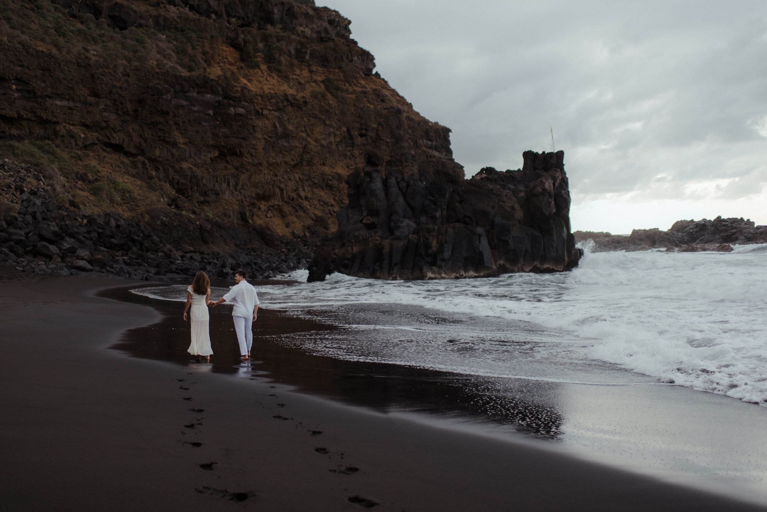 A sequence of dramatic coastal views showing waves crashing against black volcanic cliffs on a stormy beach.