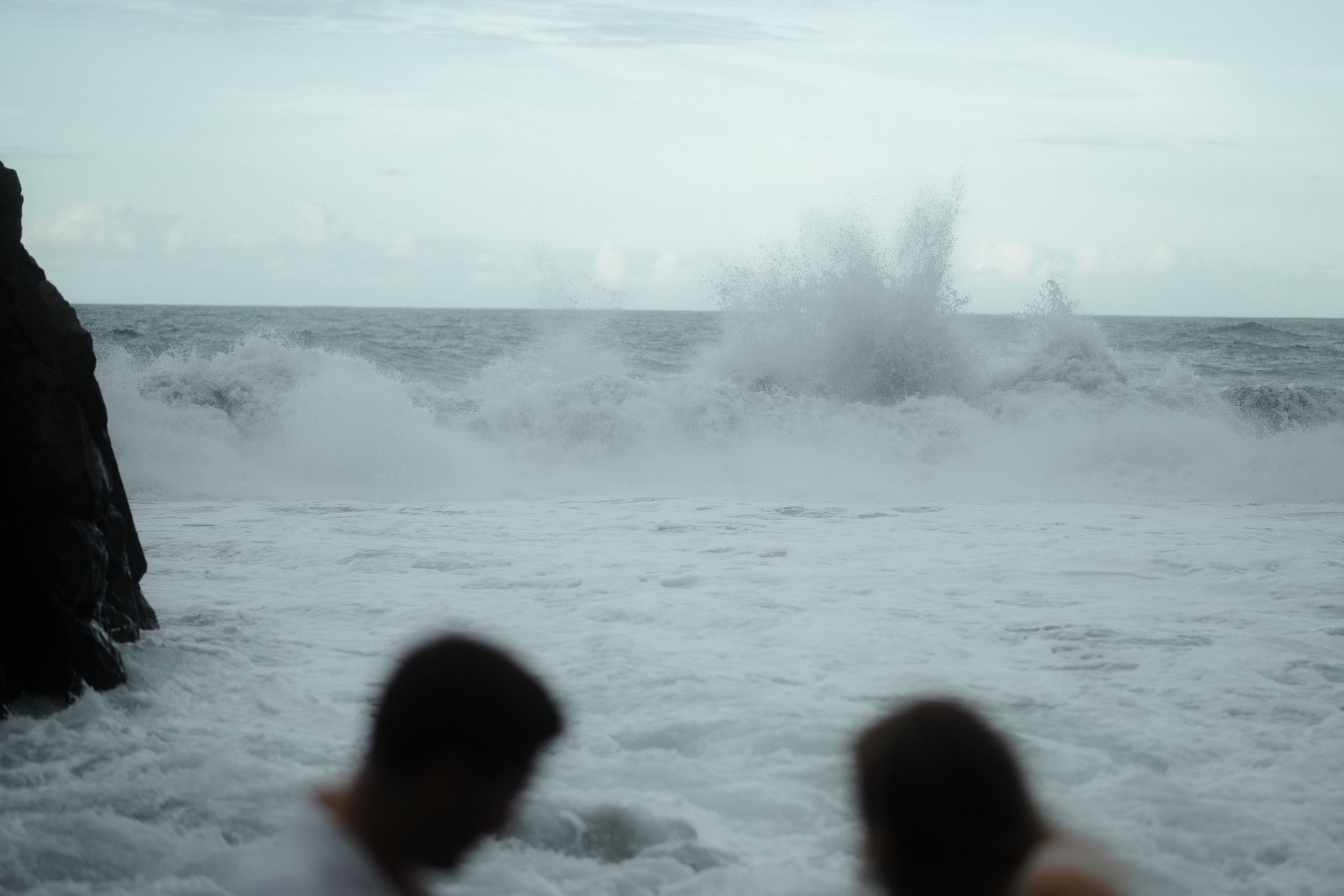 Dramatic ocean waves crash against rocks during stormy weather creating a misty seascape.