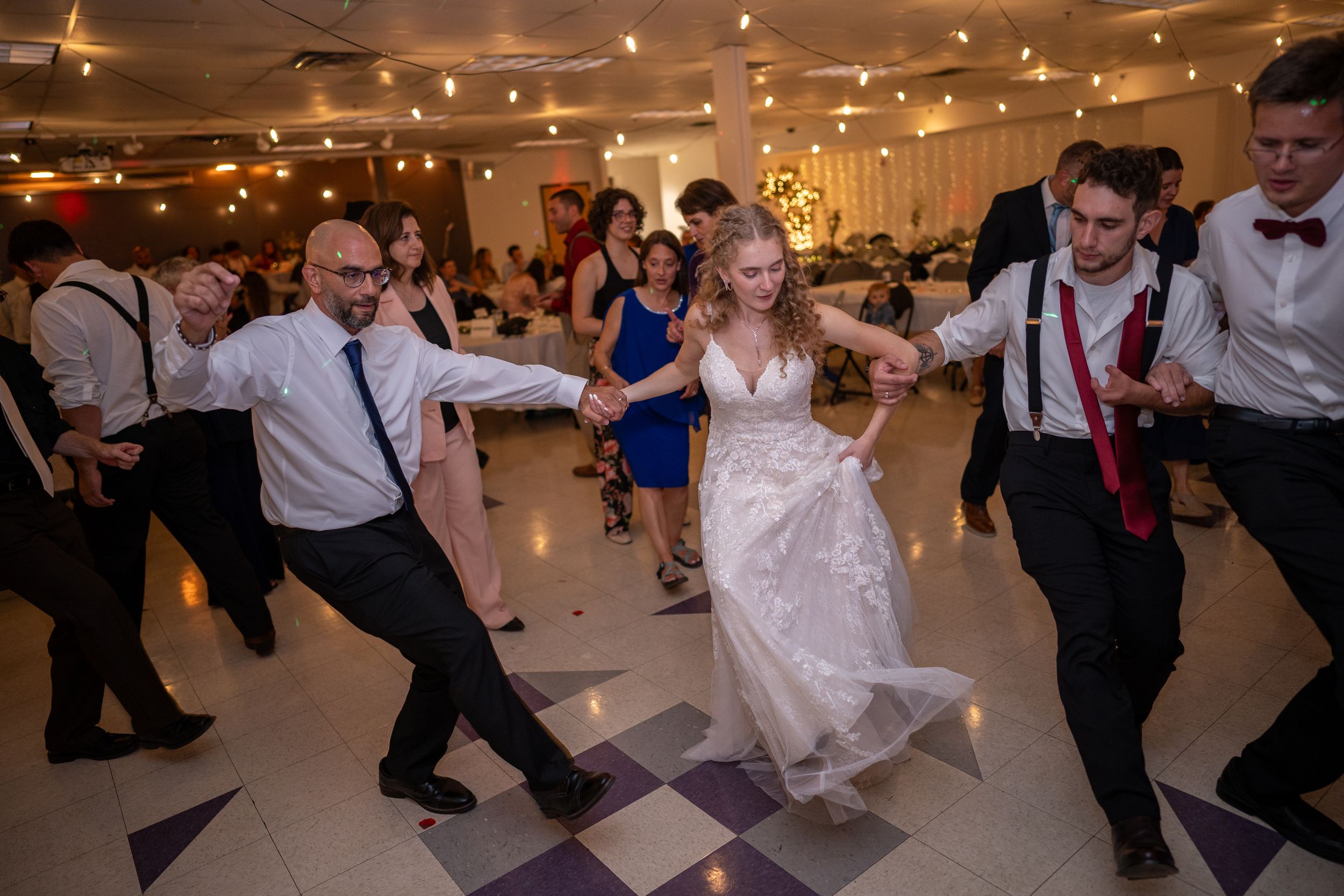 Wedding reception dance floor filled with guests dancing under string lights and decorative lighting.