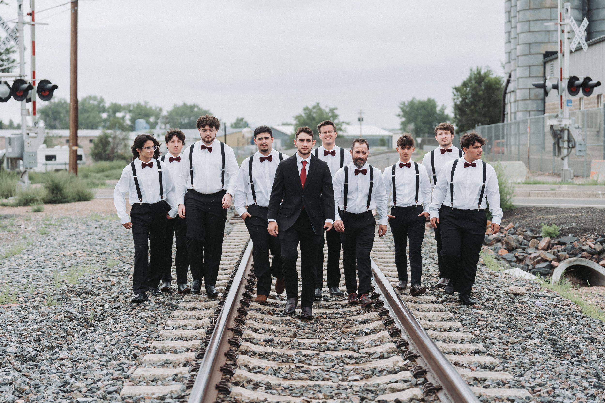 A group in formal attire poses on railroad tracks creating a stylish black and white wedding party photo.