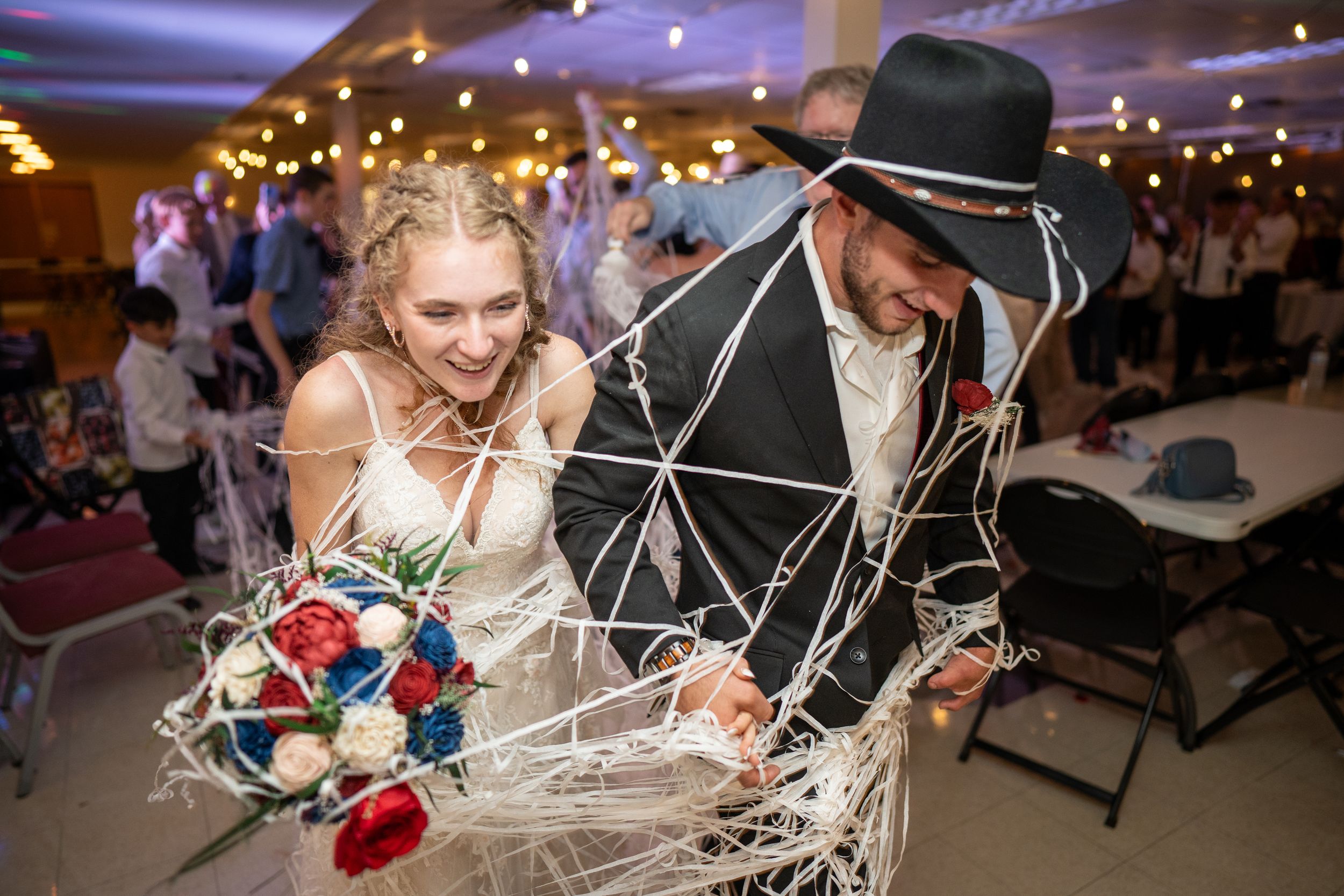 A couple in formal attire dance at a wedding reception under twinkling lights and decorations.
