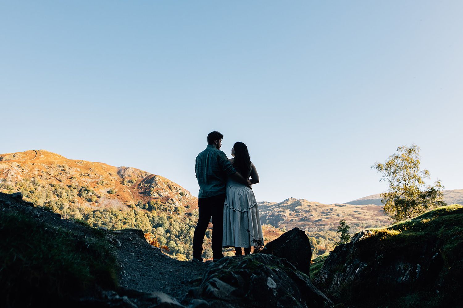 Silhouettes of a couple stand against dramatic mountain landscapes at sunset in a series of romantic outdoor photos.