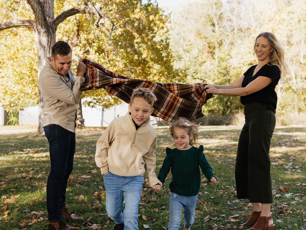 Family enjoying a playful autumn photoshoot together in a park with golden leaves and sunlight filtering through trees.