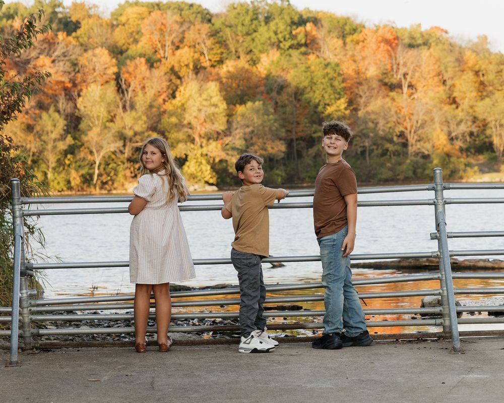 A group sits together on a white fence during autumn with golden foliage in the background.