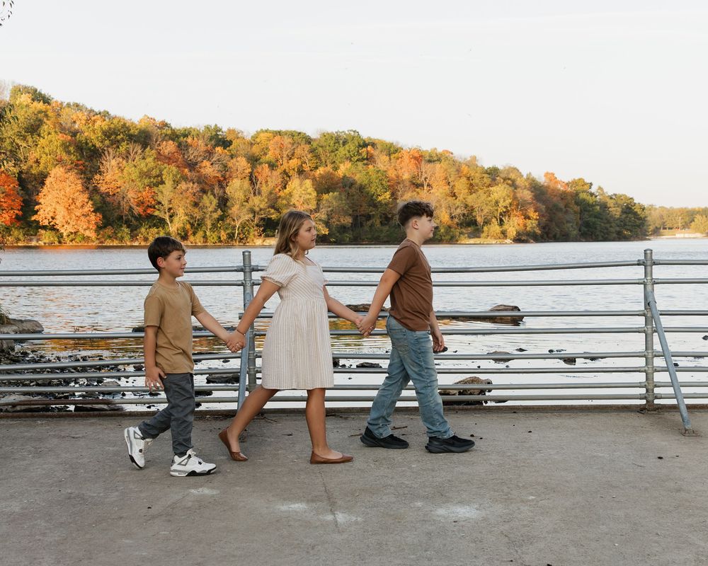 A series of people skating along a waterfront path during a golden autumn sunset.