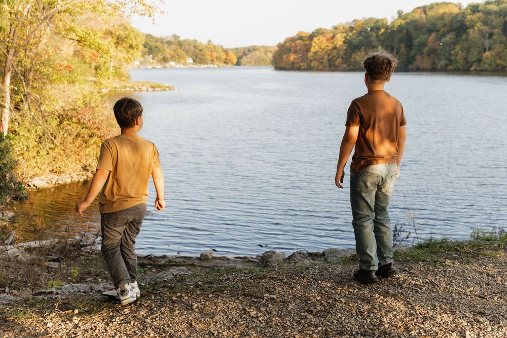 A person skips stones across a tranquil lake surrounded by autumn trees on a golden afternoon.