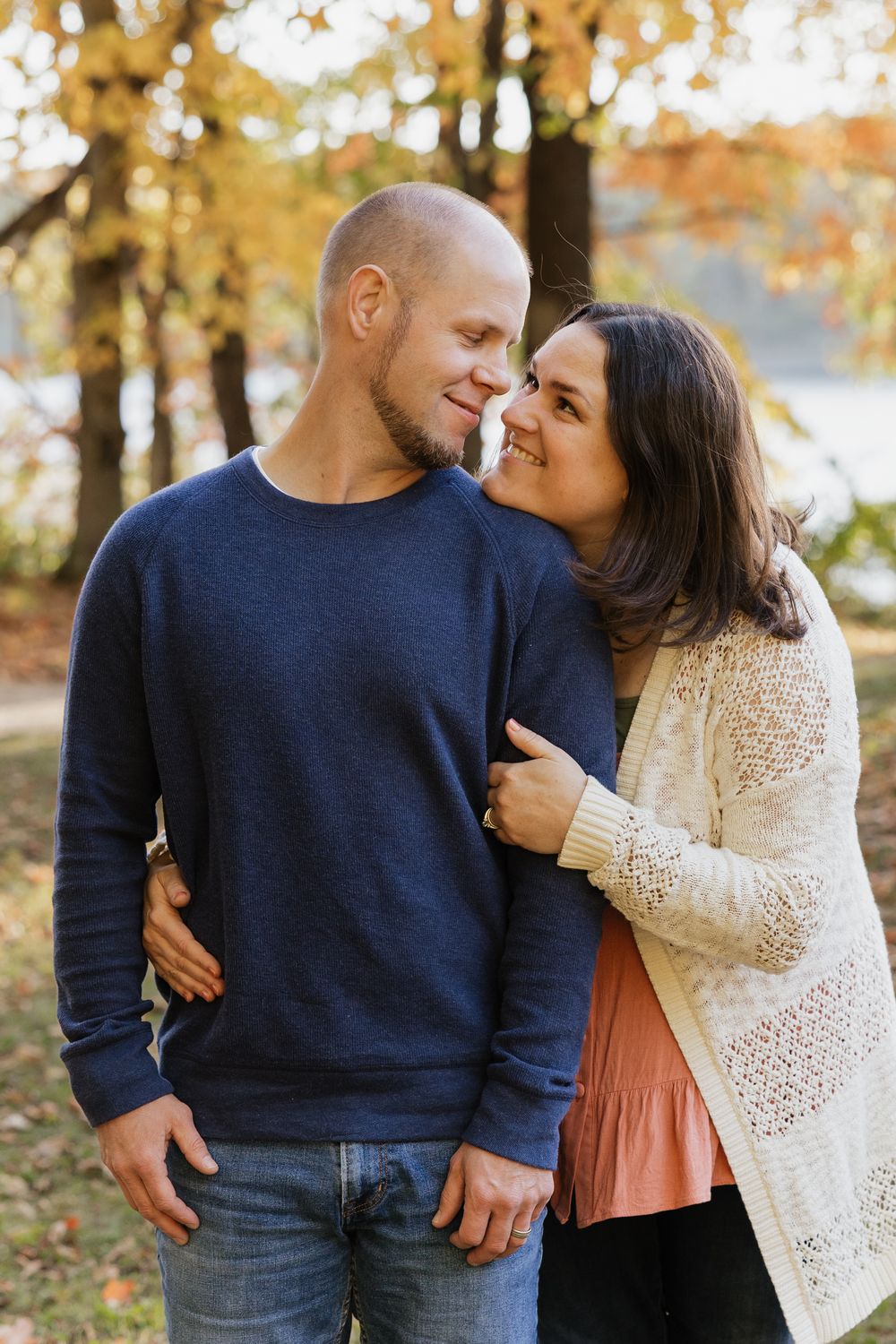 A couple shares an intimate moment outdoors during autumn with golden fall foliage in the background.