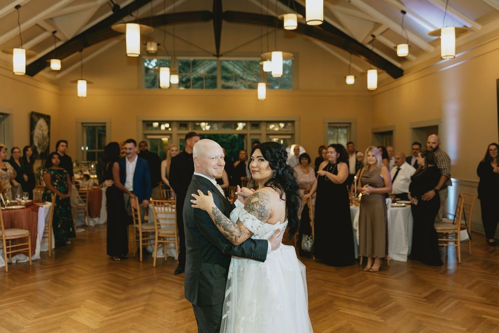Wedding guests dancing together in a large reception hall with warm lighting and hardwood floors.