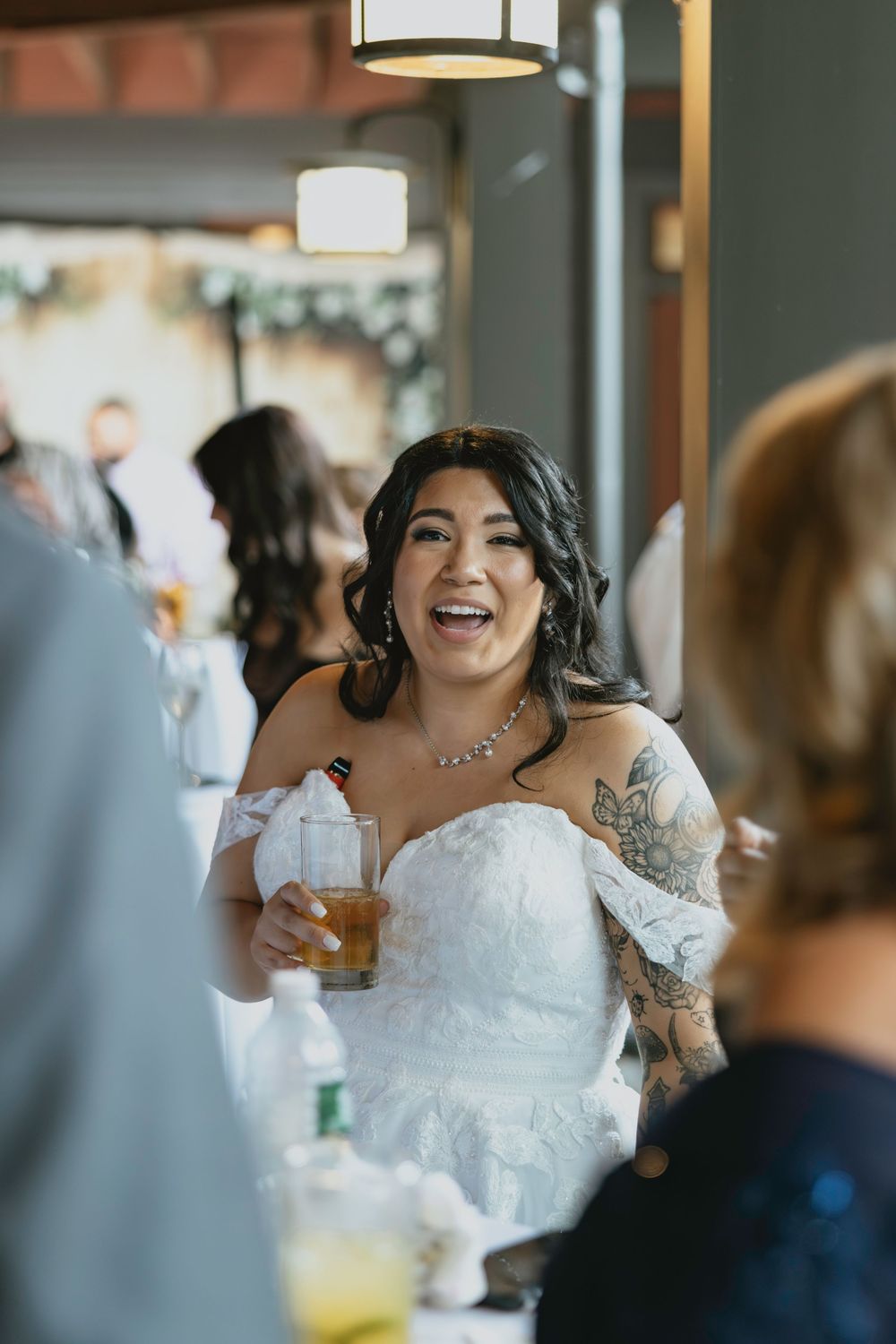 A joyful bride in a white lace wedding dress laughs during a reception celebration.