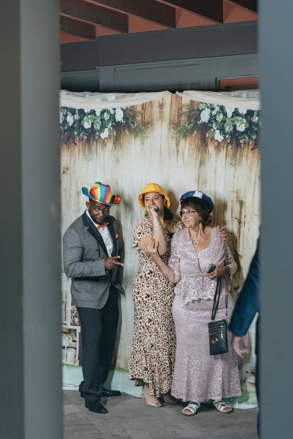 Wedding guests in formal attire gathered at an indoor venue with decorative floral backdrop.