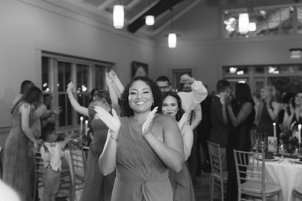 People dancing and celebrating with raised arms at a lively indoor wedding reception.