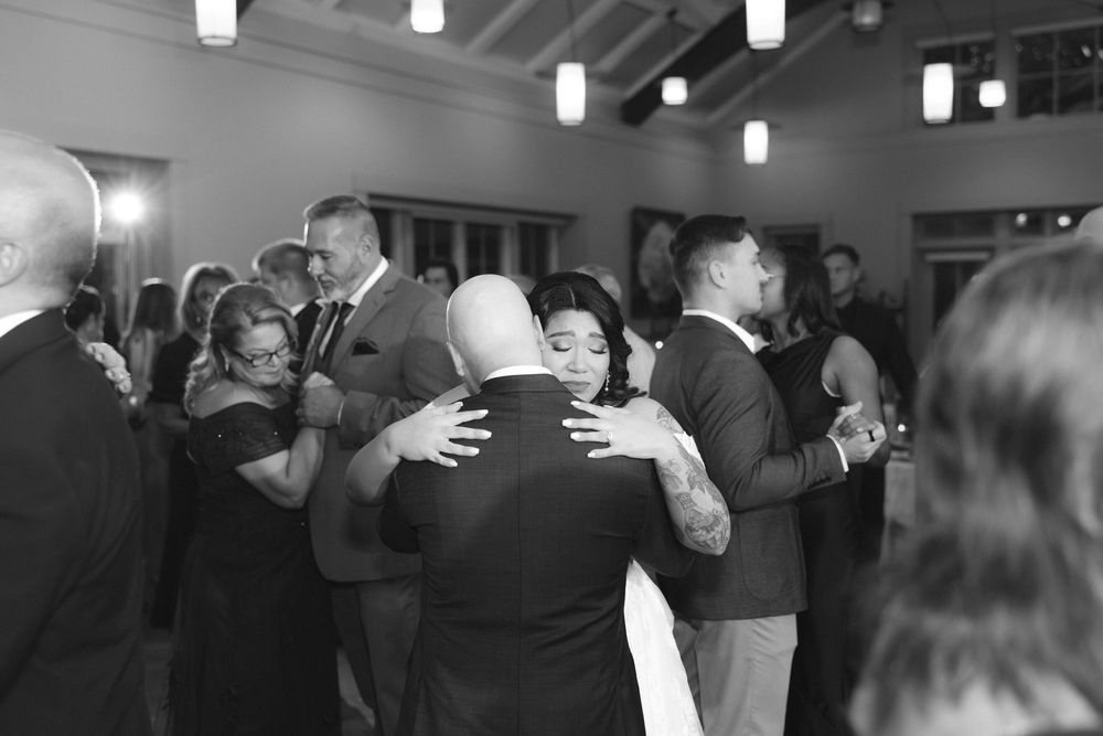 Black and white photo of couples slow dancing at an elegant indoor event with pendant lighting.
