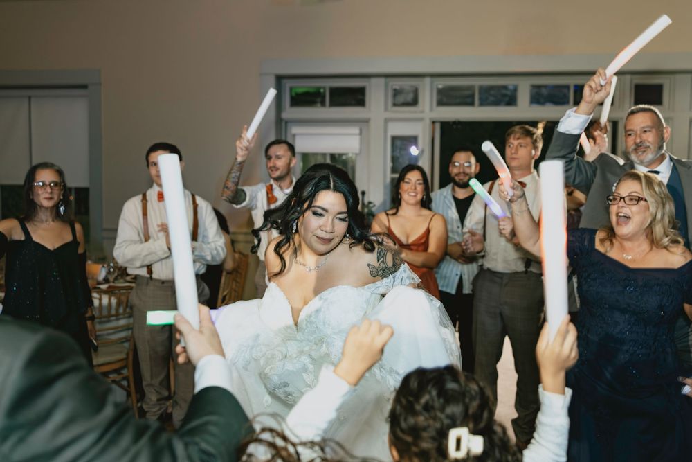 Wedding guests dance and celebrate on a crowded dance floor at an indoor reception venue.