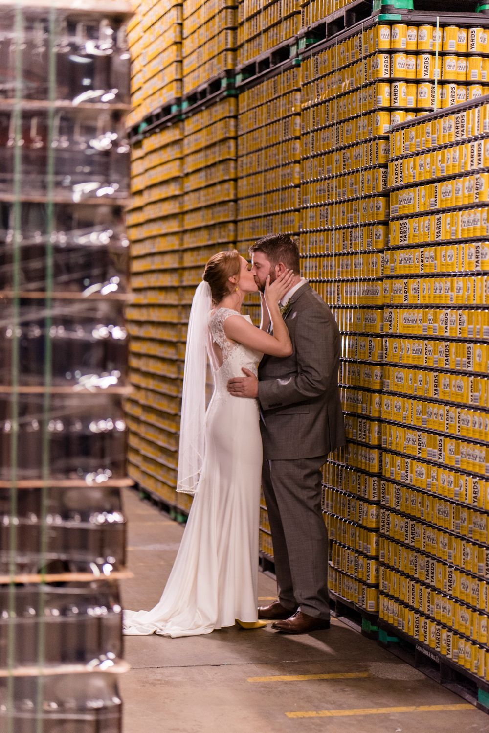 A romantic wedding couple shares intimate moments against a backdrop of storage shelves in a warehouse setting.