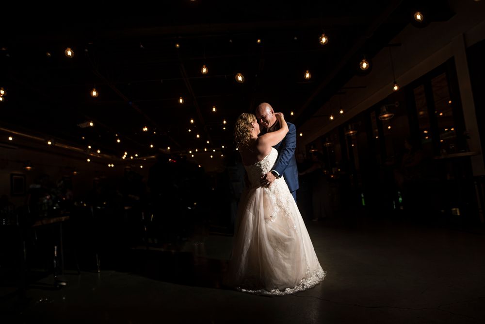 A wedding couple shares a romantic dance on a dimly lit ballroom floor surrounded by twinkling lights.