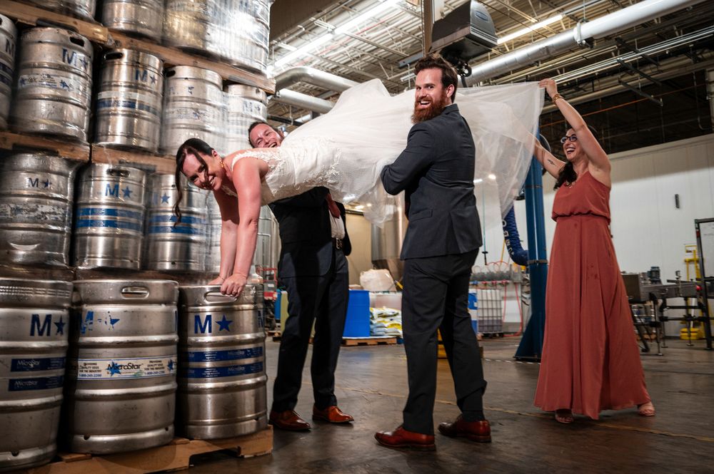 Group of people examining and tapping beer kegs in an industrial brewery warehouse setting.