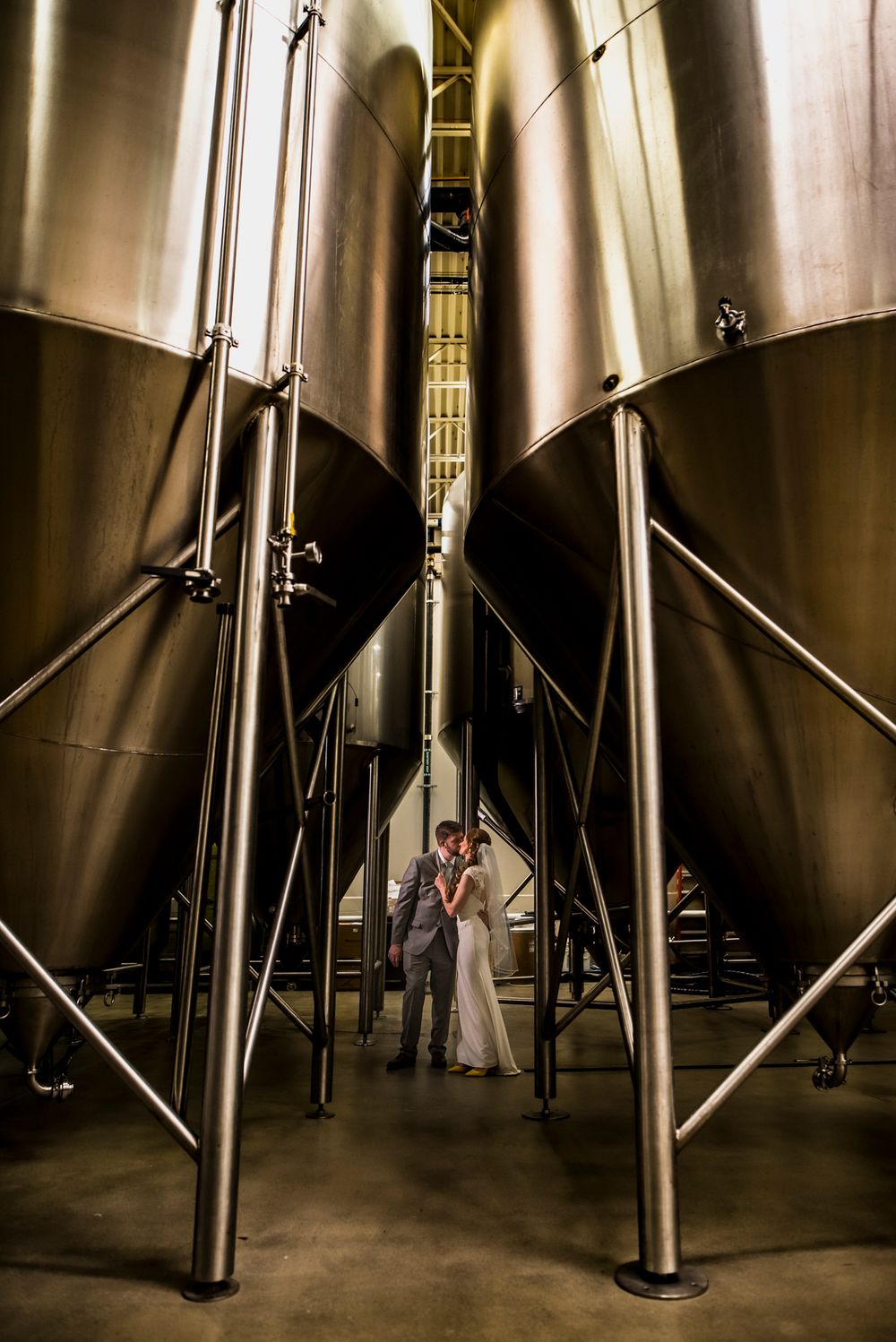 Large stainless steel fermentation tanks stand in rows at a brewery or winery facility.
