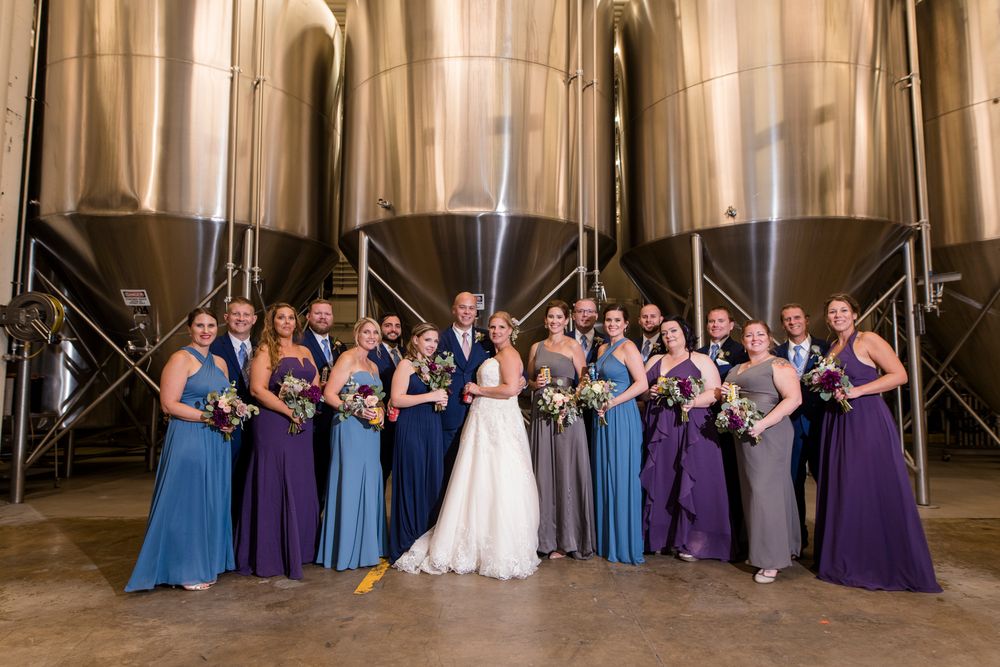 Wedding party poses together in formal attire with bridesmaids wearing purple and blue dresses.