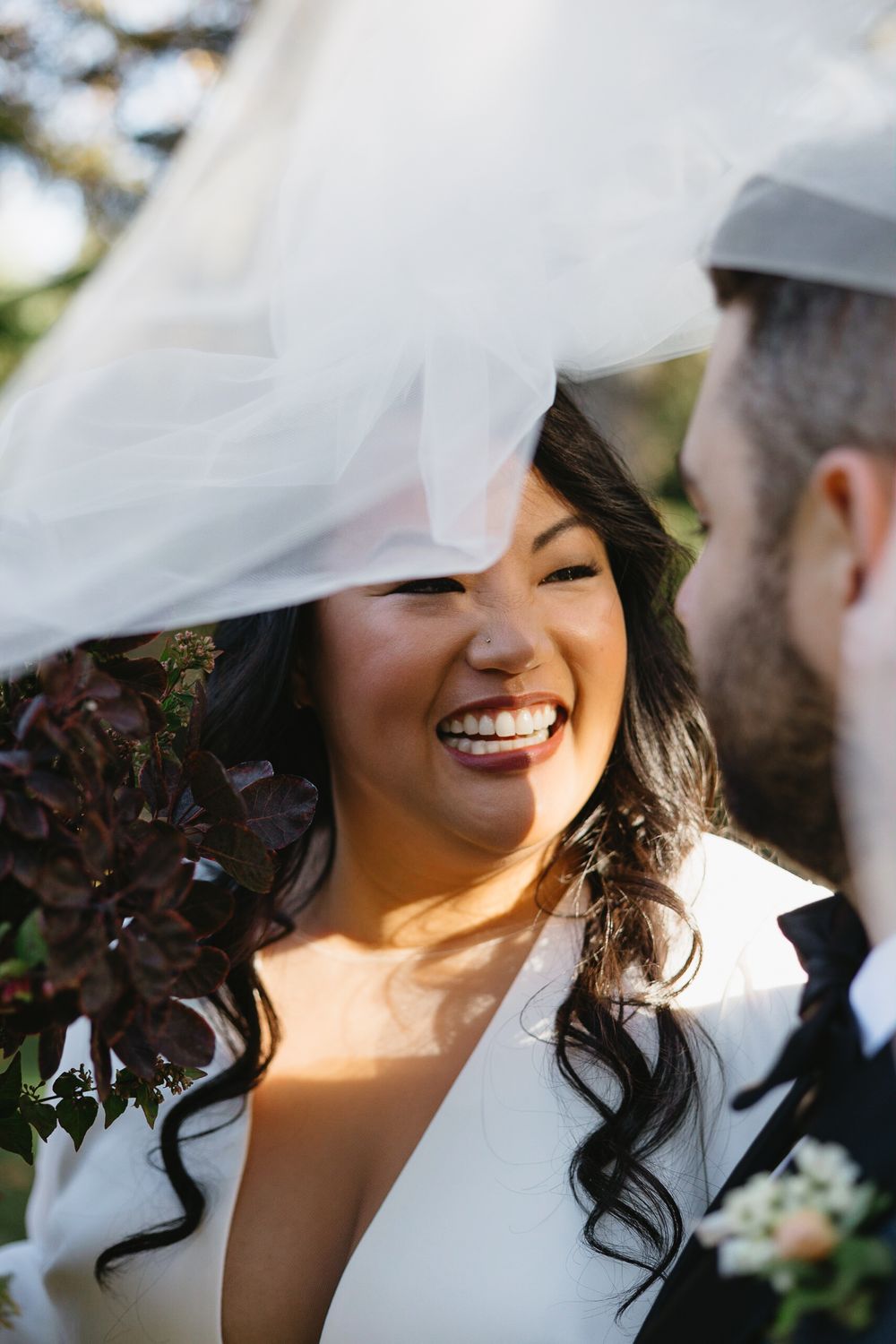 A romantic wedding moment captured under a flowing white veil as sunlight creates a soft, ethereal glow.