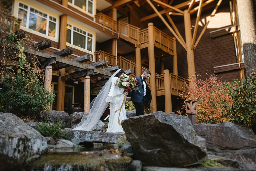 Bride and groom share a romantic moment on rocky steps outside a rustic mountain lodge venue surrounded by autumn foliage.