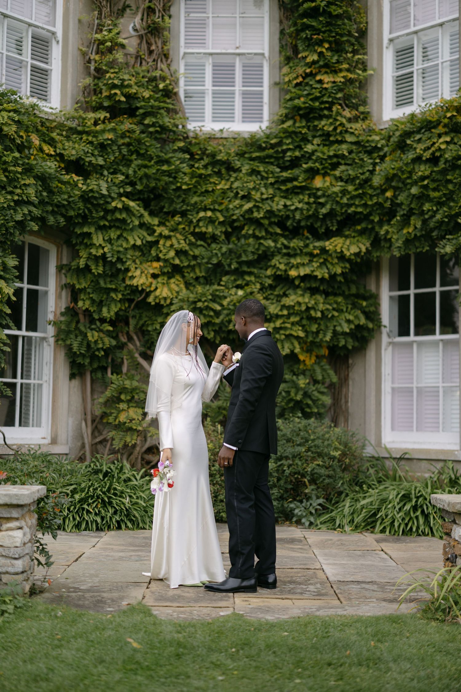 A couple in wedding attire shares a romantic moment in a lush garden setting during their outdoor ceremony.