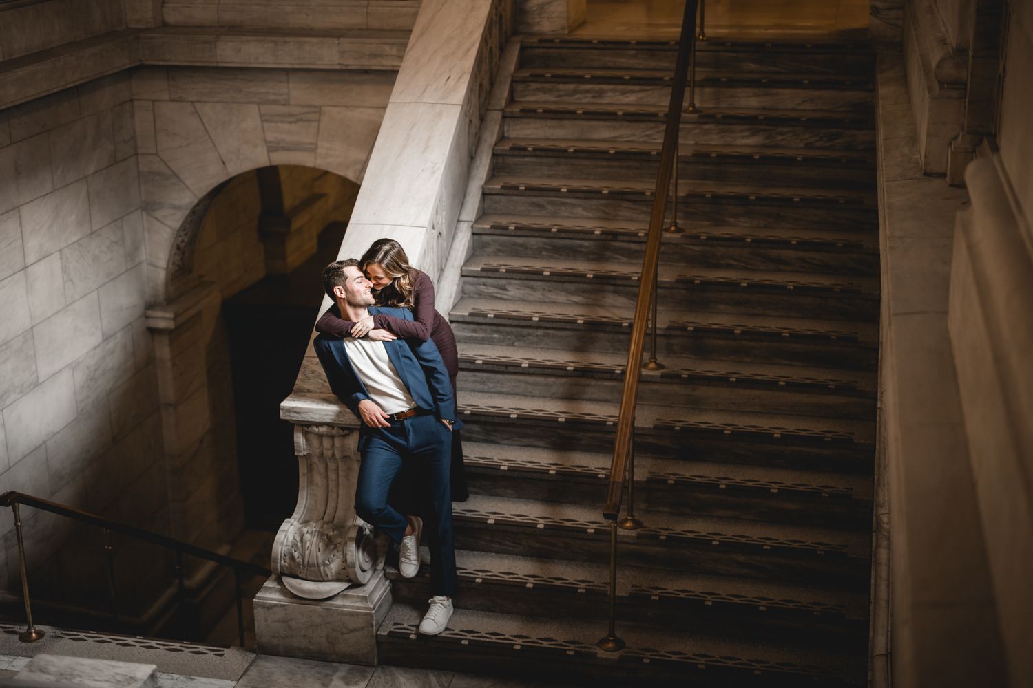 A romantic couple embraces on vintage stone stairs in an elegant architectural setting.