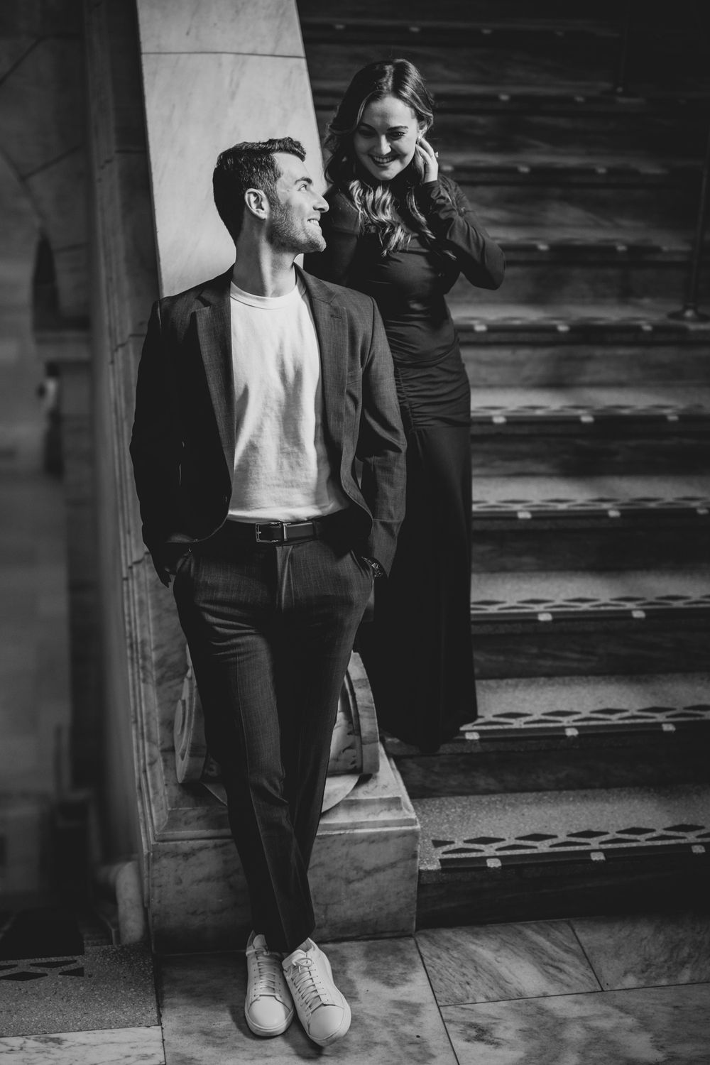 Stylish couple poses on grand stone staircase in black and white photography.