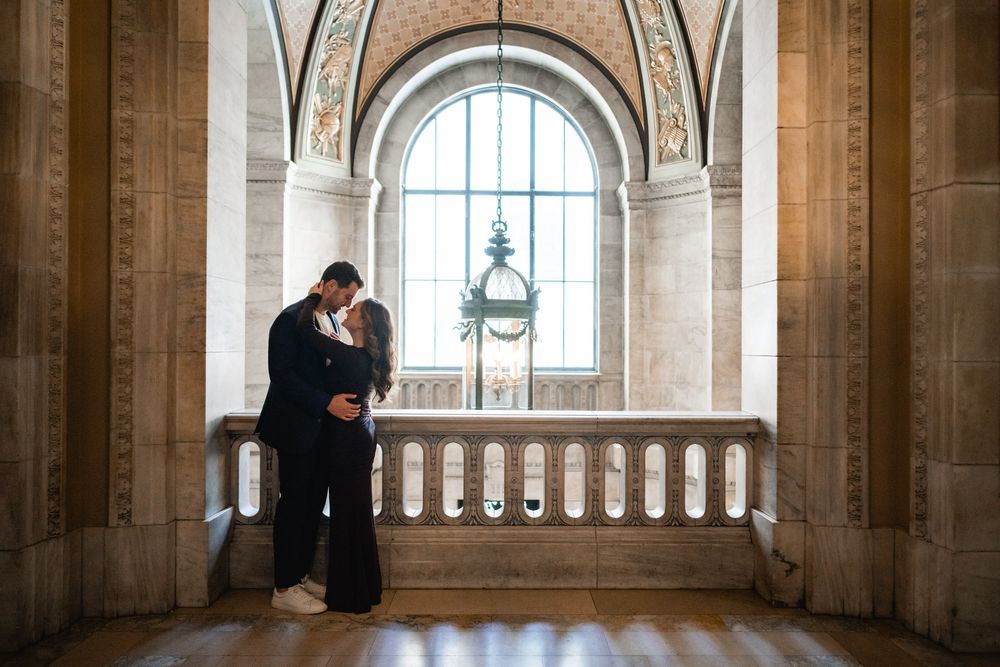 Couple shares intimate moment by arched window in ornate stone hallway.