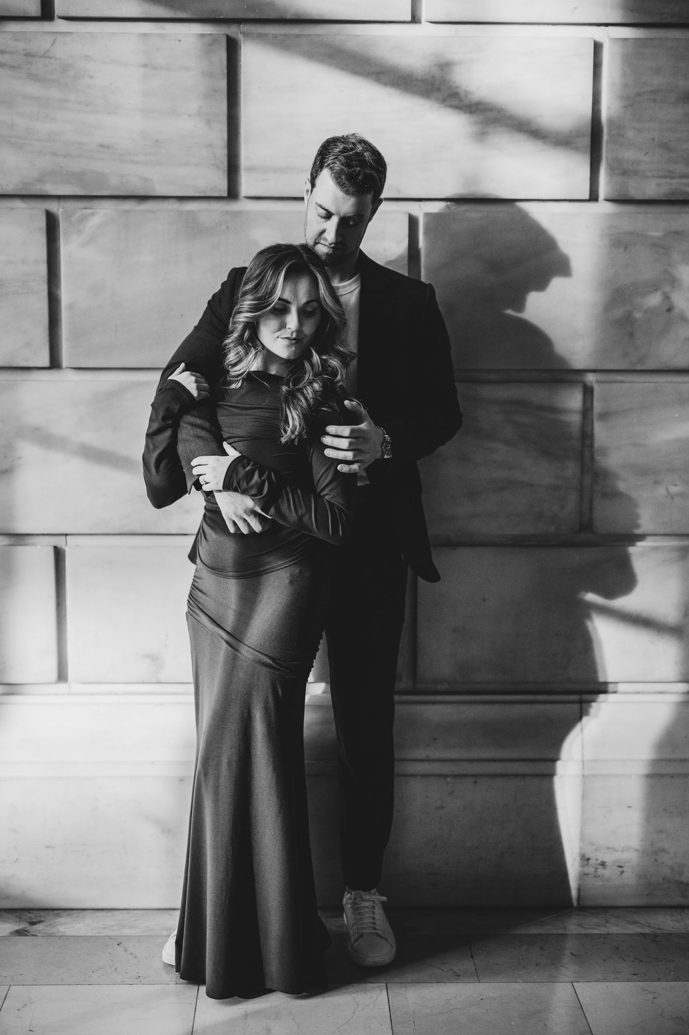 Dramatic black and white portrait of couple against stone wall with strong shadows.