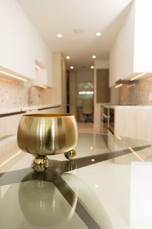 A golden decorative bowl with ball feet sits on a reflective countertop in a modern white and wood kitchen.