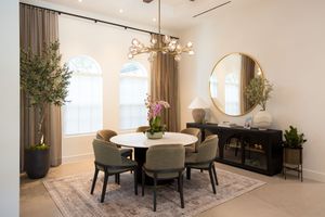 Elegant dining room with round white table, green chairs, gold mirror, chandelier, arched windows, and decorative plants on a vintage rug.