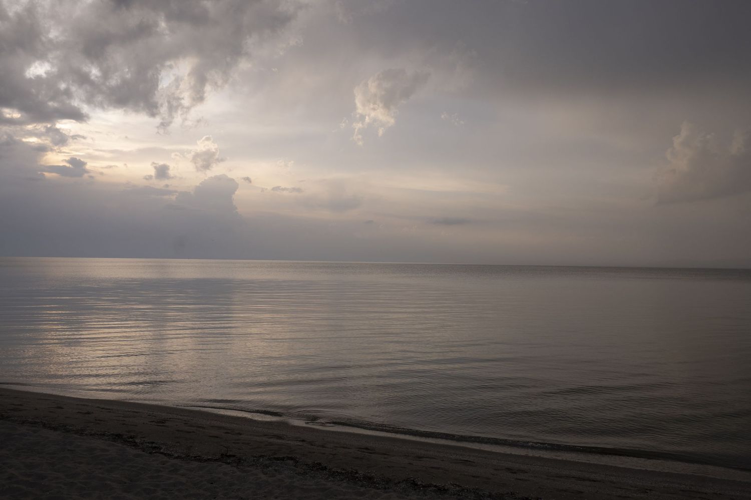 Dramatic stormy clouds hover over a calm ocean at dusk with soft light reflecting on the tranquil water's surface.