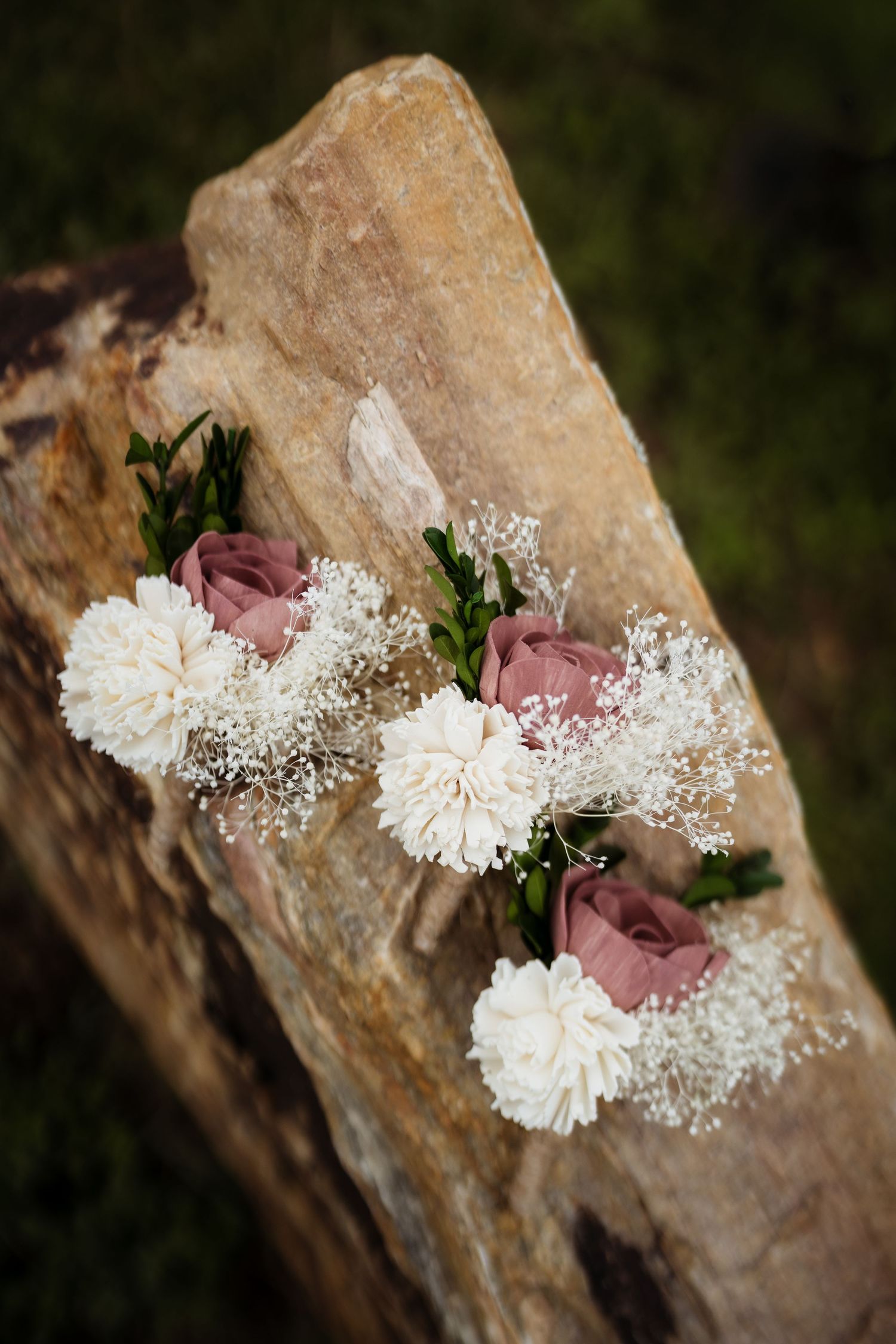 White carnations and dusty pink roses arranged with baby's breath on a rustic stone surface in natural lighting.