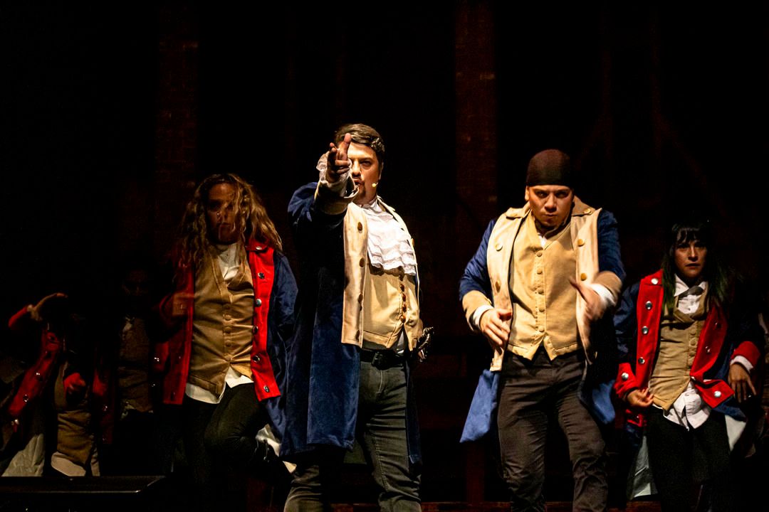 Performers on a dimly lit stage during a theatrical production with dramatic lighting effects.