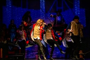 Theater actors performing on stage with dramatic blue lighting and silhouetted figures in motion.