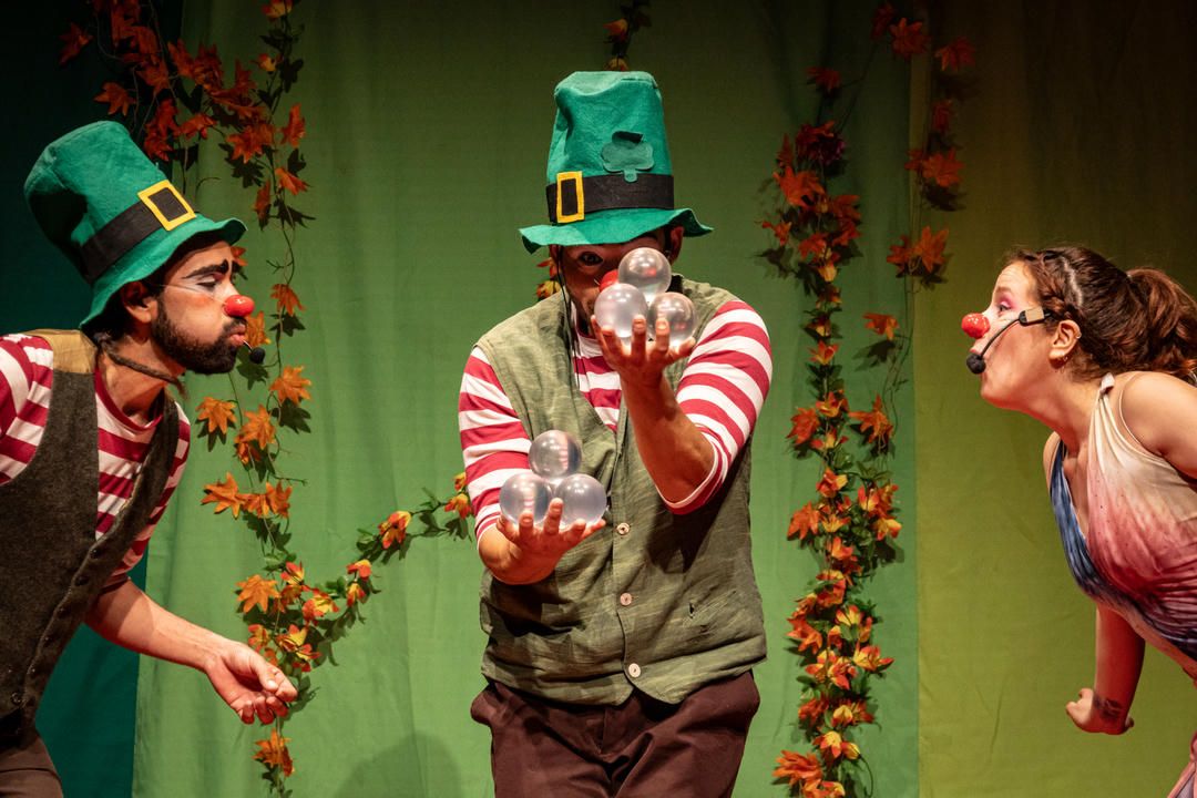 A whimsical holiday scene with performers in green hats and striped stockings against a leafy backdrop.